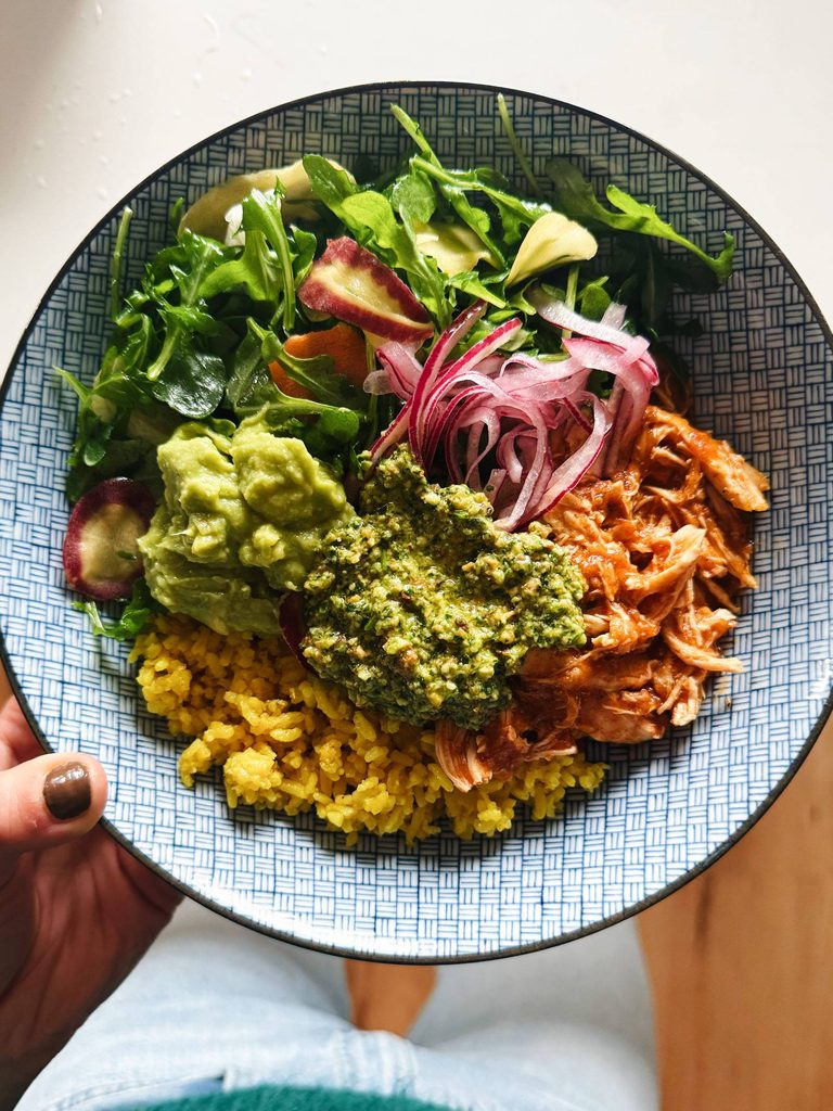 Crockpot chicken in a bowl with yellow rice, greens, onions, and cilantro pesto.