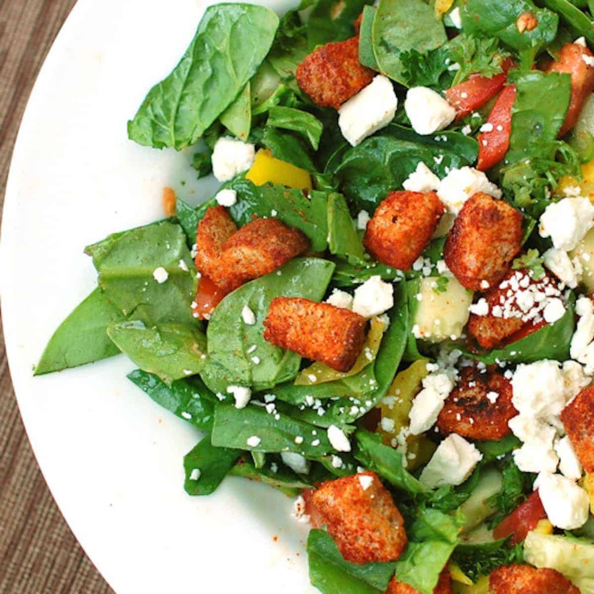Greek salad with fresh spinach, tomatoes, cucumbers, banana peppers, parsley, feta cheese, and homemade paprika croutons.